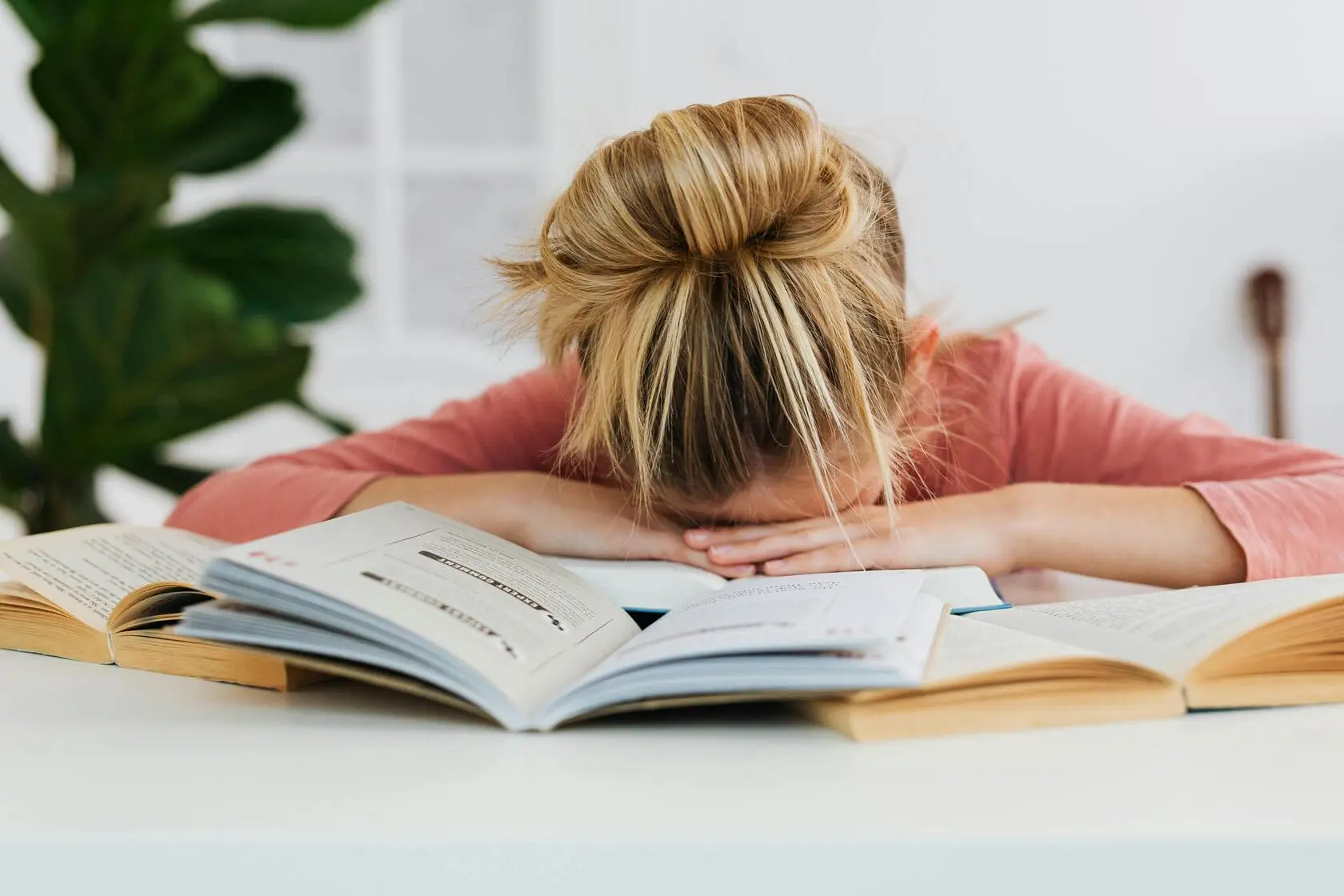 Estudante sem rotina de sono descansando a cabeça sobre livros abertos durante a preparação para medicina