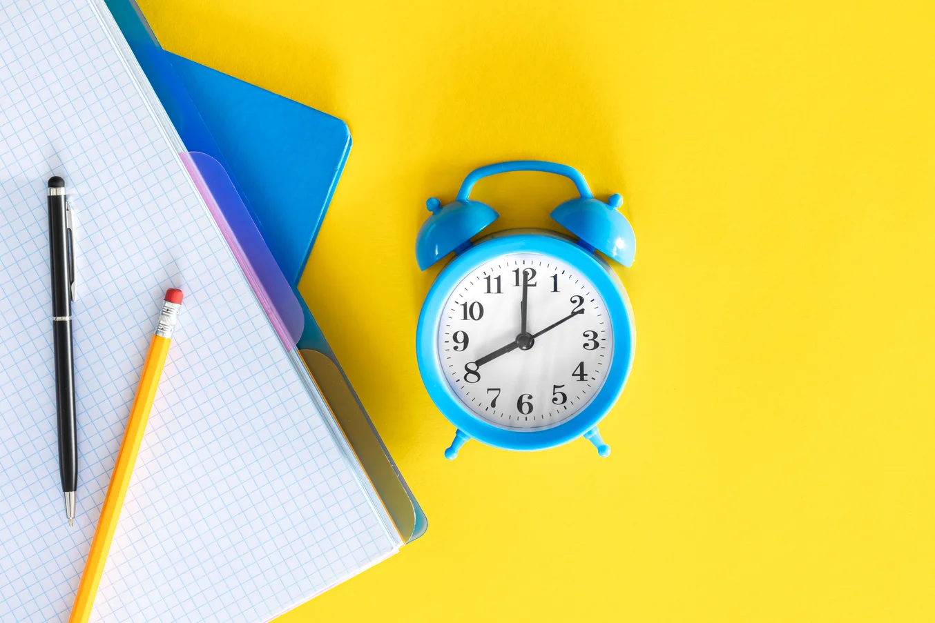 Relógio azul e materiais de estudo sobre fundo amarelo, representando a busca pelo melhor horário para estudar para o ENEM e Medicina
