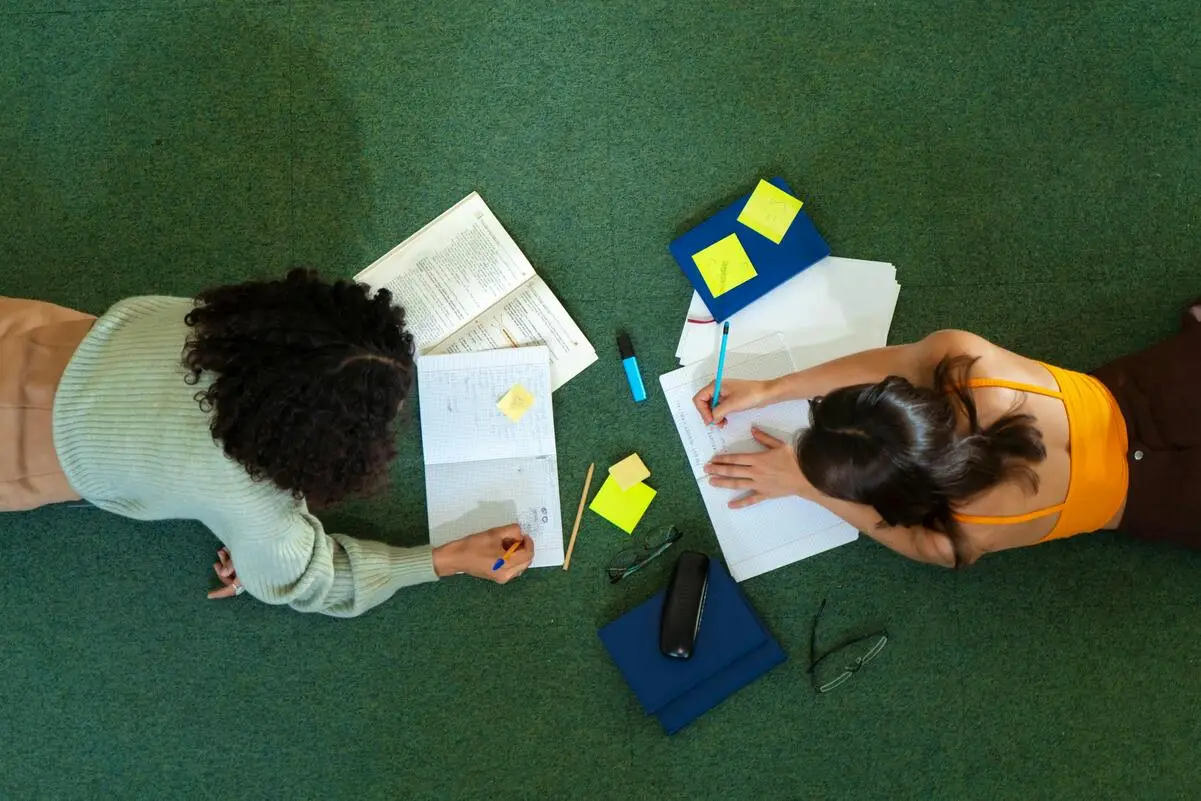 Duas estudantes vistas de cima revisando matéria para o ENEM com cadernos, post-its e livros espalhados no chão