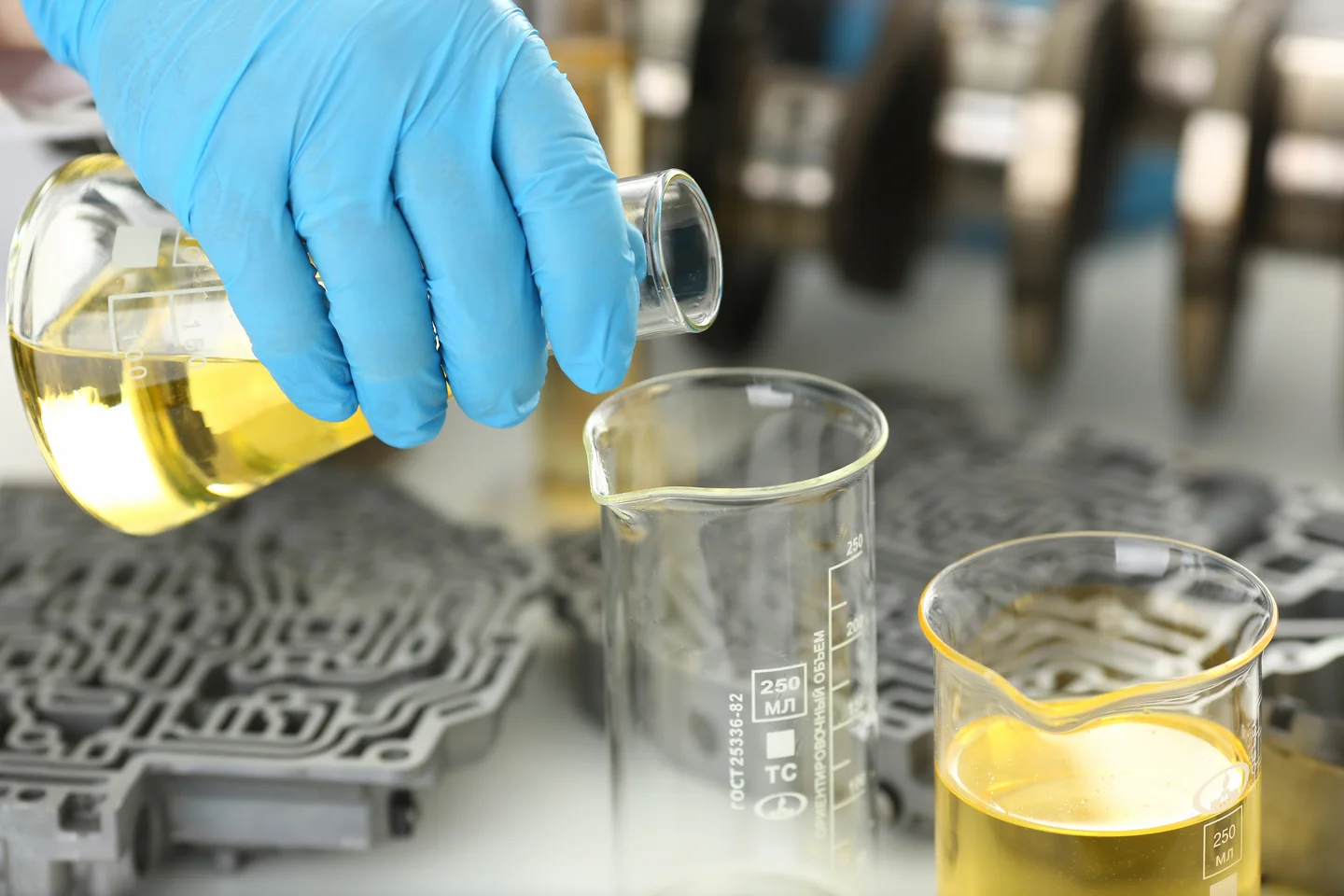 Mão com luva azul transferindo líquido amarelo entre béqueres em experimento de separação de misturas em laboratório.