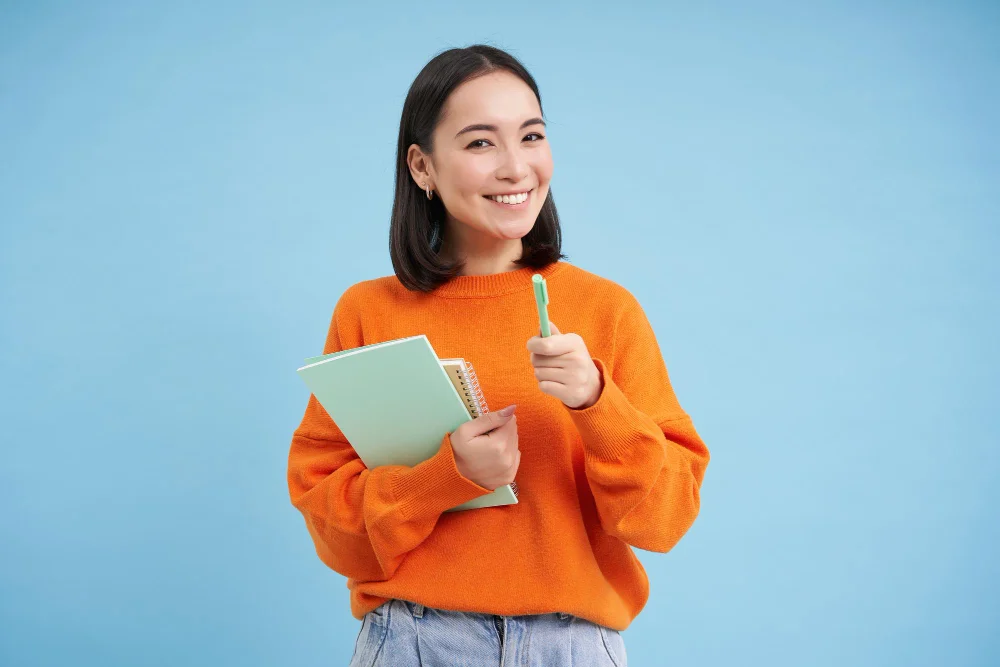 Estudante sorrindo com caderno e caneta na mão após anotar a data do ENEM 2026 confirmada pelo edital oficial do INEP.