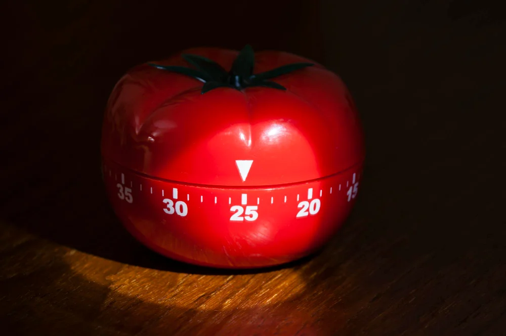 Timer clássico em forma de tomate sobre superfície escura representando a técnica pomodoro para estudar com foco e pausas programadas.