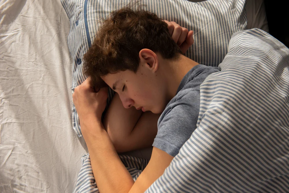 Jovem dormindo profundamente na cama, representando a relação entre sono e rendimento nos estudos e a consolidação da memória durante o descanso.