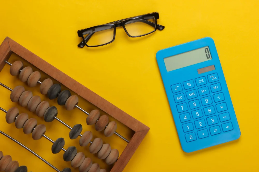 Ábaco, calculadora e óculos sobre fundo amarelo representando o estudo de funções no ENEM
